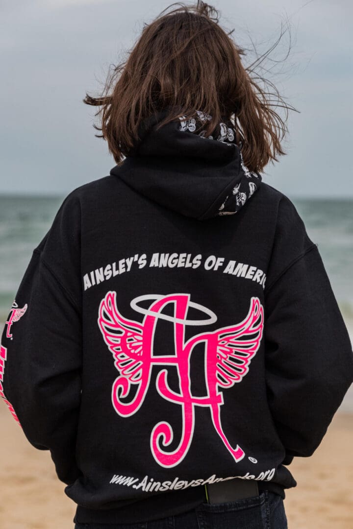 short-haired woman wearing a black Ainsley’s Angels of America hoodie at the beach