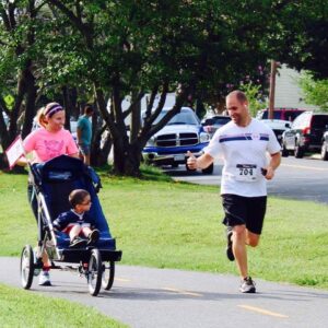 man running and doing an ok sign to a child in a jogger chair