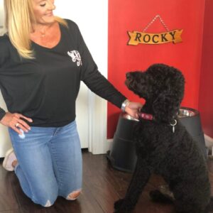 a woman wearing a black, long sleeved Ainsley’s Angels of America shirt and her black poodle