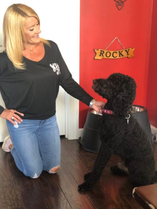 a woman wearing a black, long sleeved Ainsley’s Angels of America shirt and her black poodle